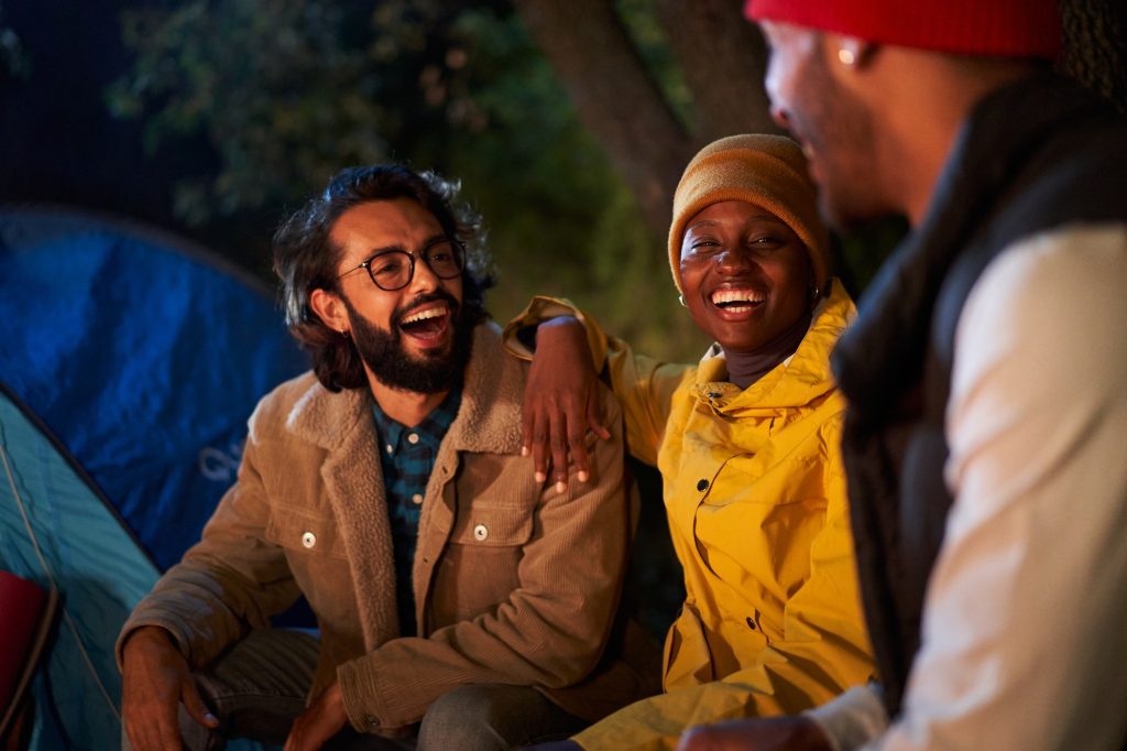 Three multiracial young people enjoying at outdoor winter camping trip. Friends laughing together.
